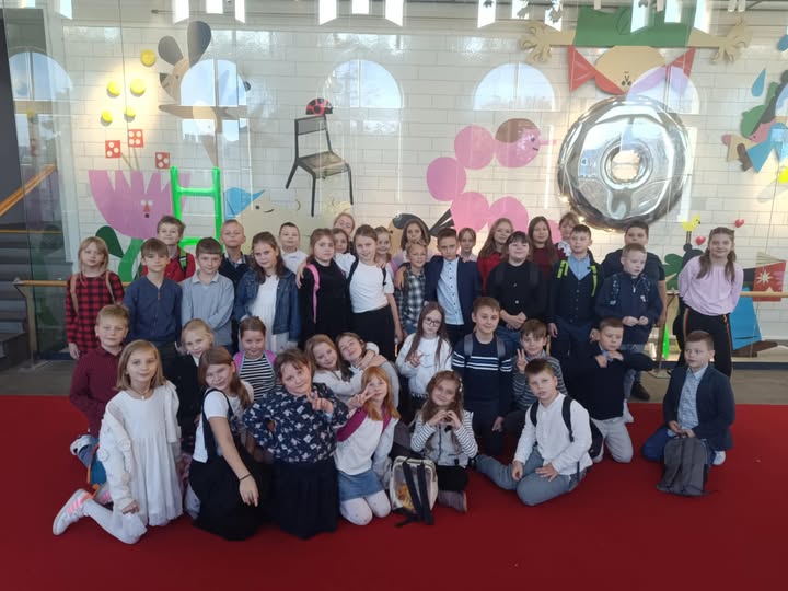 Uczniowie klas 3a i 3b pozują wspólnie do zdjęcia na tle kolorowej, bajkowej dekoracji w Teatrze Arlekin.