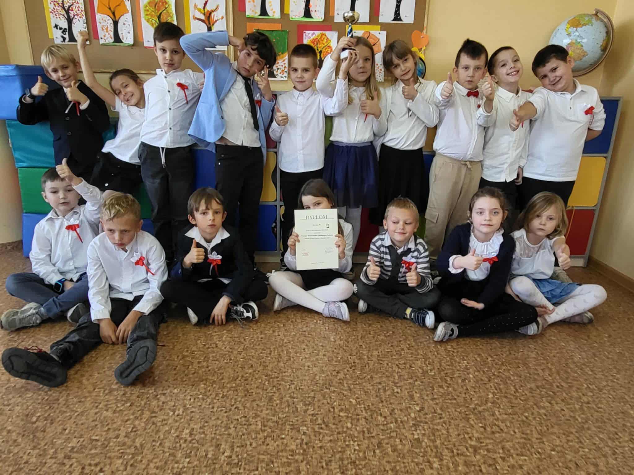 Uczniowie klasy 1b z SP 13 w Pabianicach pozują z dyplomem i pucharem za zwycięstwo w Stefankach; dzieci odświętnie ubrane, siedzą i stoją, pokazując kciuki do góry.