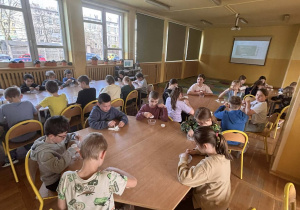 Grupa dzieci pracuje przy stołach w sali świetlicowej.