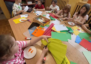Dzieci przy stole wycinają kolorowy papier i tworzą prace plastyczne.