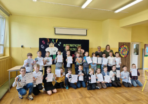 Grupa uczniów stoi razem z dyplomami po zakończeniu konkursu matematycznego.