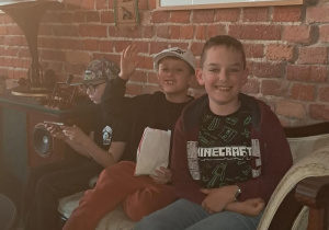Uczniowie odpoczywają na zabytkowej kanapie podczas zwiedzania atrakcji edukacyjnej.