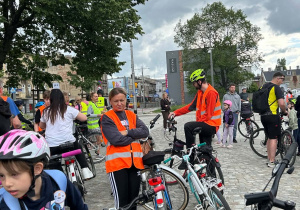 Uczestnicy rajdu rowerowego z rowerami i kaskami gromadzą się przed startem na placu w centrum miasta.